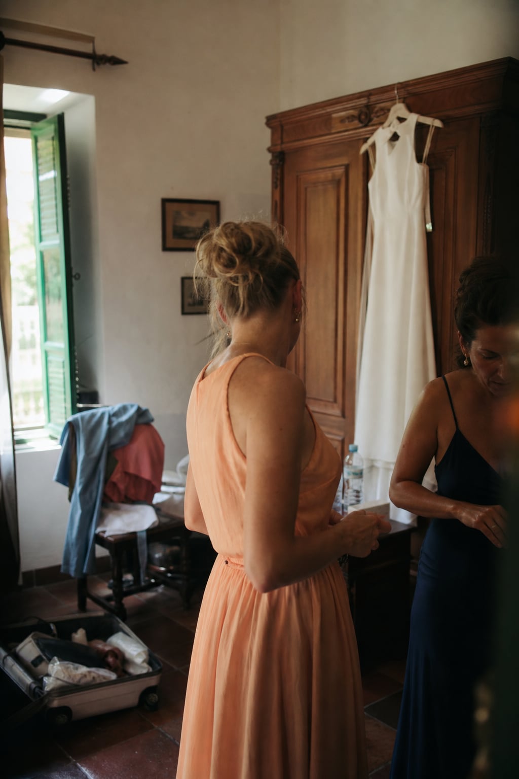 Damas de honor preparándose junto al vestido de novia colgado en un armario antiguo
