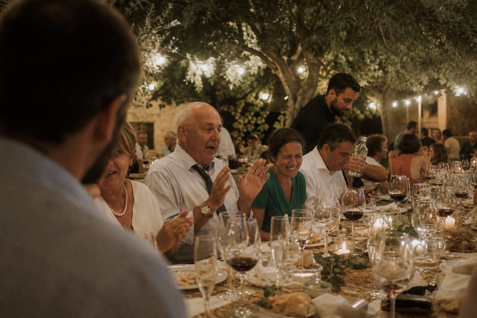 Invitados riendo en una larga cena de boda bajo los olivos de una finca en Alicante